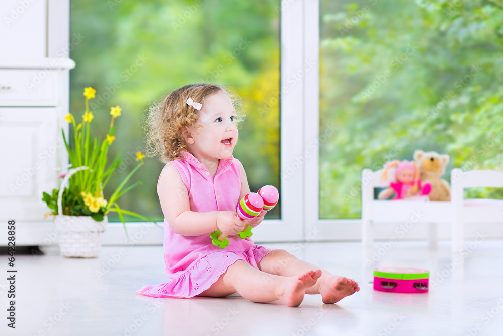 Cute curly toddler girl playing tambourine in a sunny white room Cute curly toddler girl playing tambourine in a sunny white room