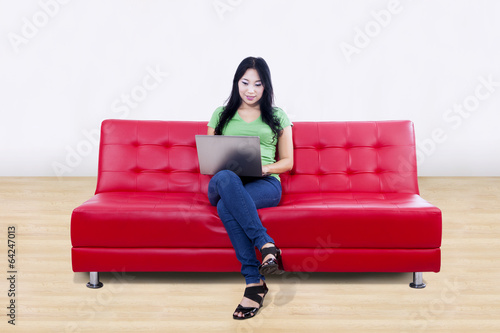 Beautiful female using laptop on red sofa at home