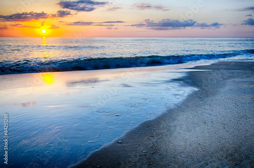 Fotografi The rising sun peeks through clouds and is reflected in waves by