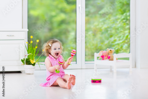 Funny toddler girl playing tambourine in sunny white room