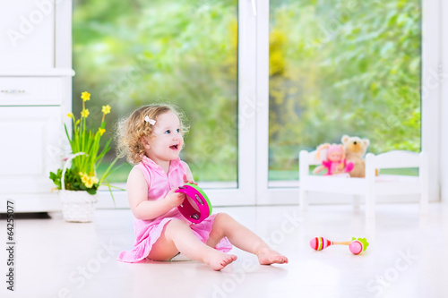 Adorable toddler girl playing tambourine next big window