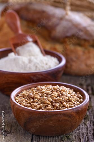 Bowl of wheat and flour withl the bread on a wooden table