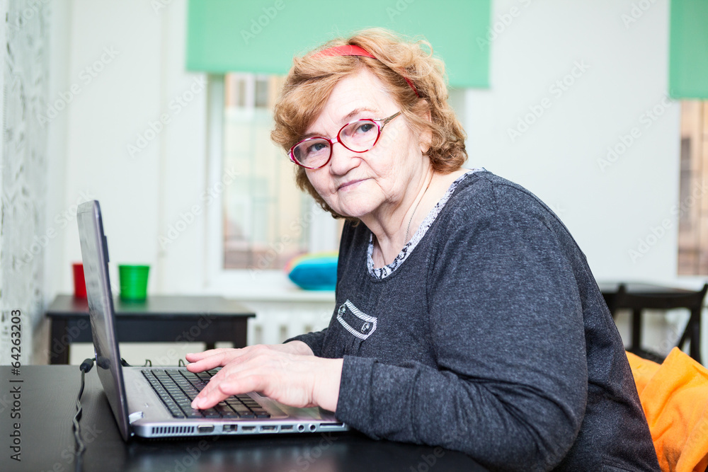 Senior age woman sitting at table with laptop, looking at camera Senior age woman sitting at table with laptop, looking at camera