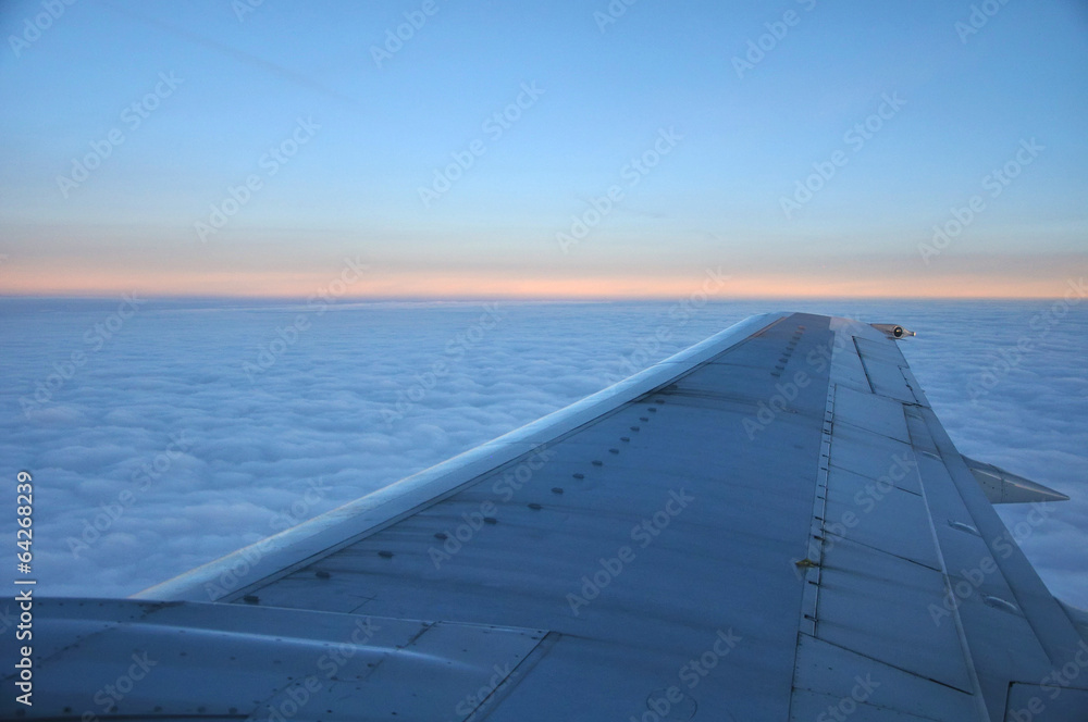 airplane wing above morning clouds and sunrise