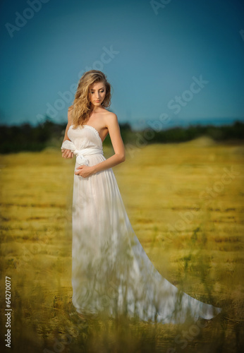 Young woman in white long dress standing on a wheat field 