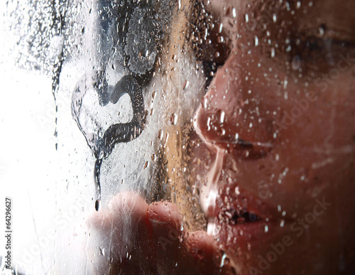 A girl slooking through the wet glass