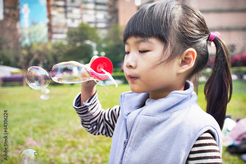The girl blowing bubbles on the grass in the park.