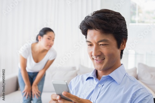 Man sending a text while girlfriend watches from couch
