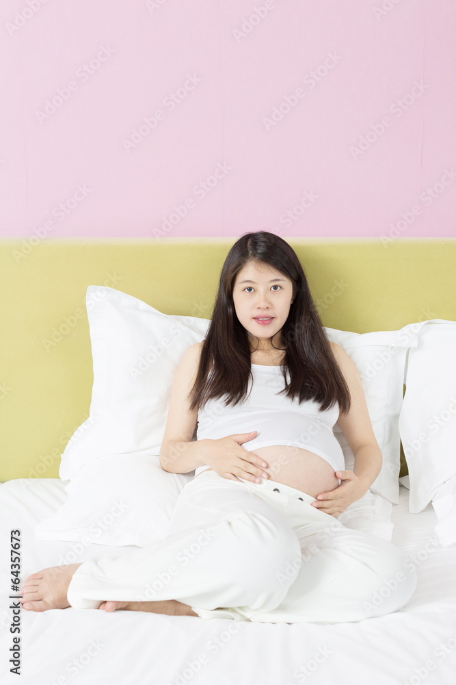Beautiful pregnant woman posing while lying on a bed at home Beautiful pregnant woman posing while lying on a bed at home