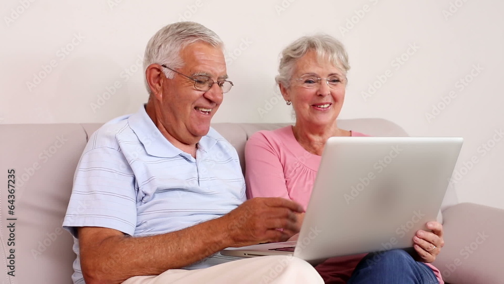 Senior couple sitting on sofa using laptop Senior couple sitting on sofa using laptop
