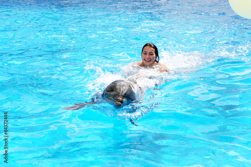 Happy beautiful young girl laughs and swims with dolphins in blu