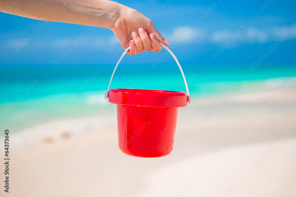 Close up hand holding a small red bucket on tropical beach Close up hand holding a small red bucket on tropical beach