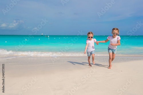 Little girls running along the white beach and having fun