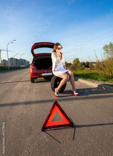 woman sitting on spare wheel against of broken car