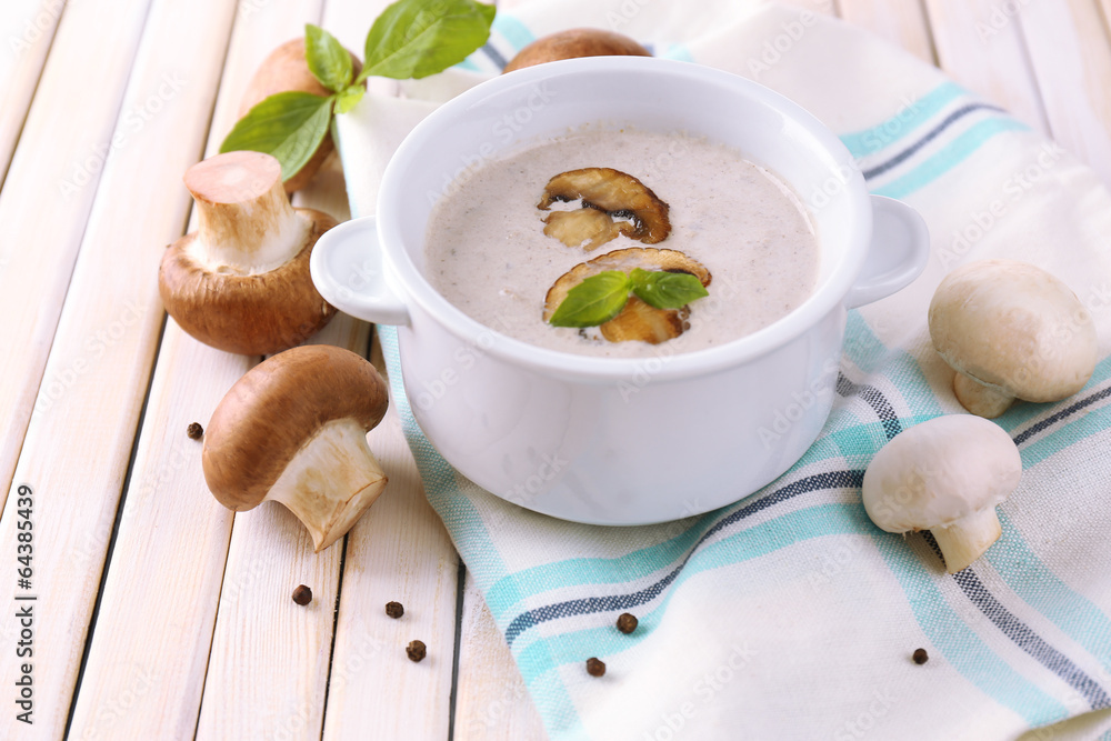 Mushroom soup in white pot, on napkin, on wooden background