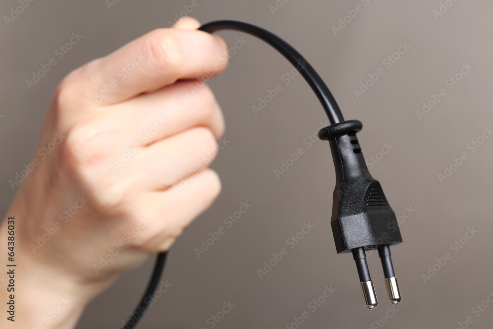 Hand holding electric plug on grey background Hand holding electric plug on grey background