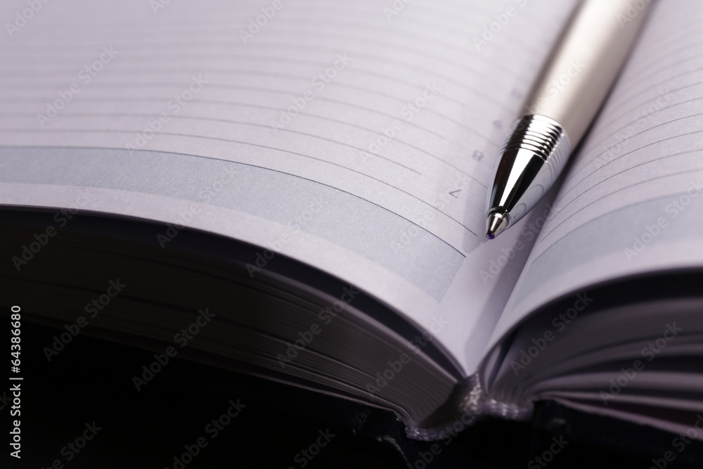 Pen on opened book on black table, close up Pen on opened book on black table, close up
