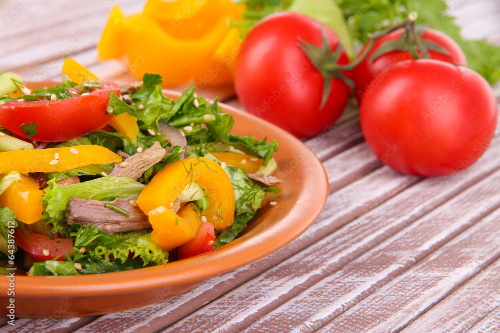 Beef salad on plate with vegetables on wooden background