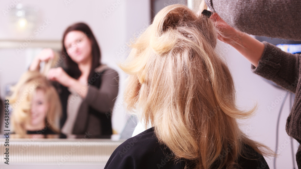 Fototapeta premium Smiling girl with blond wavy hair by hairdresser in beauty salon