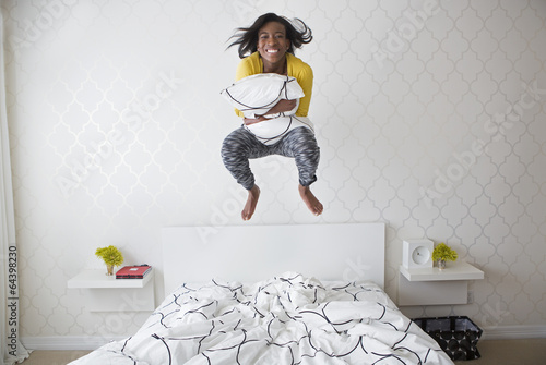 A young girl jumping high in the air above her bed. photo