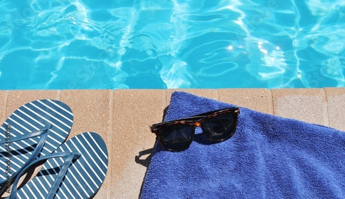 Poolside sunglasses towel holiday vacation background scenic sunglasses shoes with copy space on swimming pool water for vacation or holiday stock photo photograph image  photo