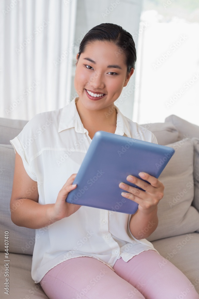 Smiling woman sitting on couch using tablet pc