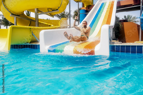 A man rolls down a hill in a aquapark on a bright sunny day