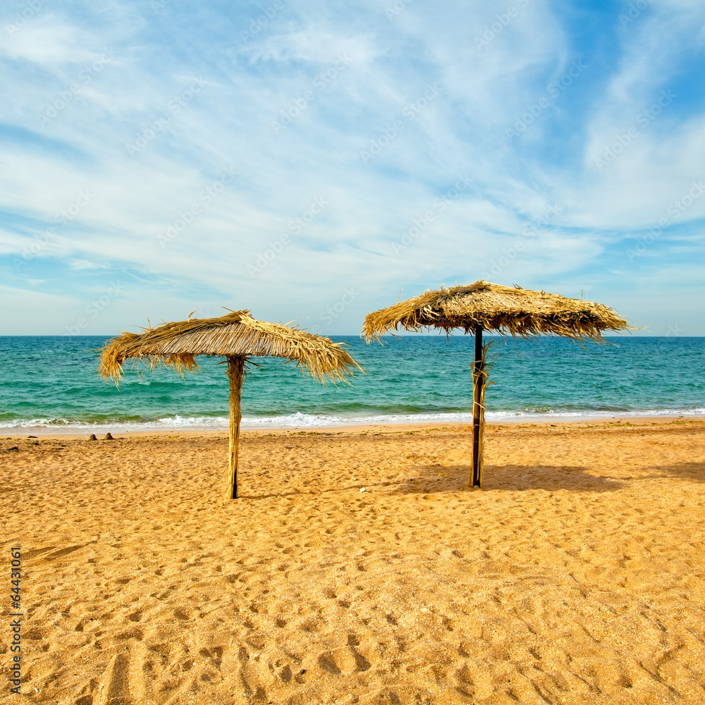 Tropical beach scenery with two straw parasols