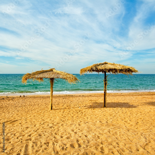 Tropical beach scenery with two straw parasols