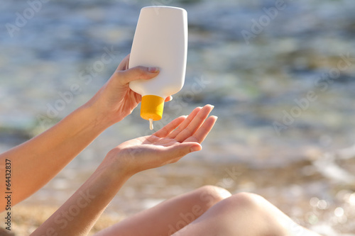 Woman hands putting sunscreen from a bottle on the beach