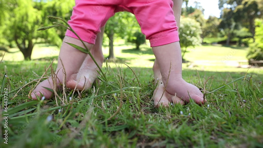 Baby walking on mothers feet on the grass