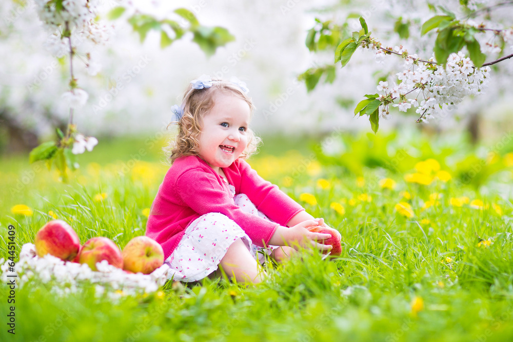 Pretty little girl eating apple inspring blooming garden
