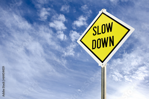 Slow Down yellow road sign against blue sky and clouds