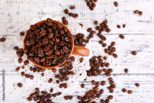 Cup full of coffee beans on light wooden background