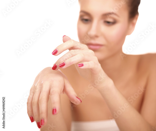 A beautiful woman is applying cream on her face over white.