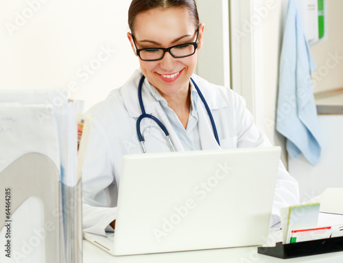 A female doctor sitting on the desk with laptop.