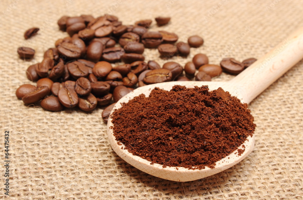 Ground coffee on wooden scoop and grains in background Ground coffee on wooden scoop and grains in background