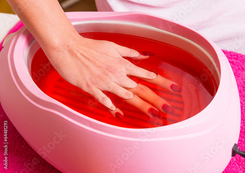 Photo Female hand and orange paraffin wax in bowl.