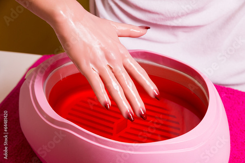 Female hand and orange paraffin wax in bowl.   
