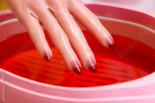 Fotografia Female hand and orange paraffin wax in bowl.