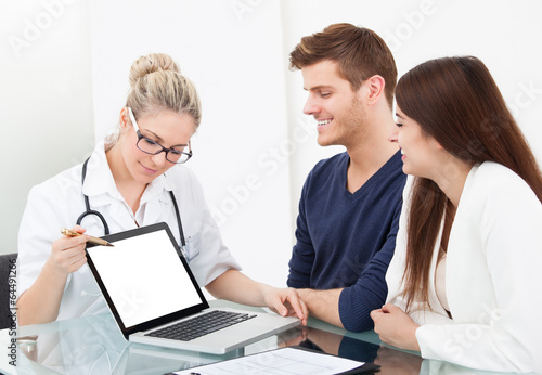 Doctor Showing Report To Couple On Laptop