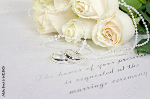 white roses and rings on wedding invitation