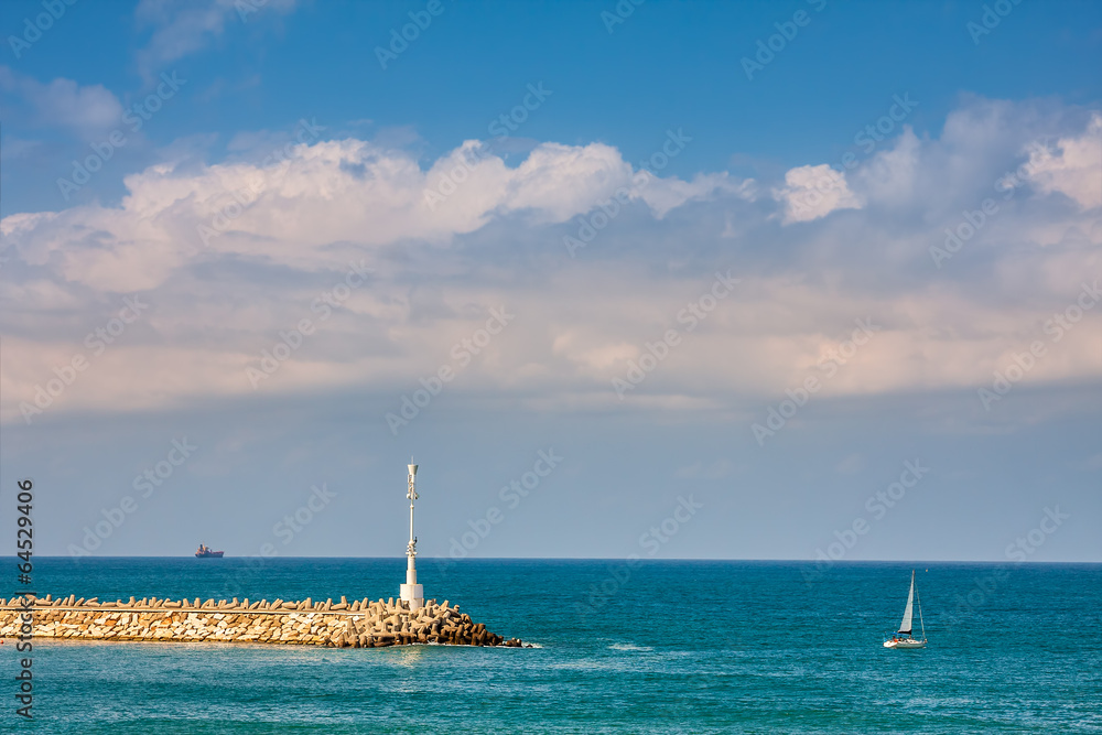 Breakwater with beacon and yacht on Mediterranean sea.
