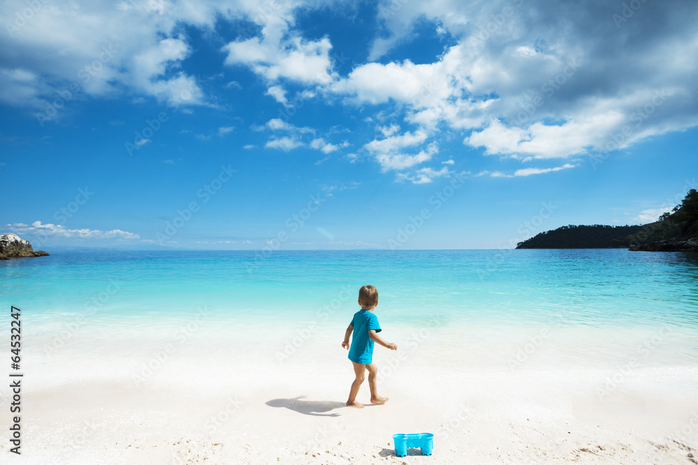 LIttle boy walking on the beach, looking at the sea.