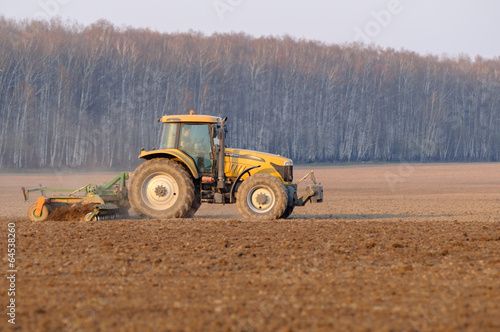 Tractor cultivates field on the background of the forest spring