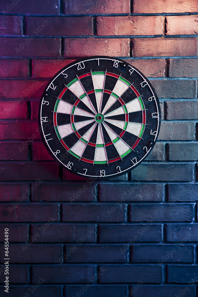 Fototapeta premium Dart board on a brick wall with dramatic lighting