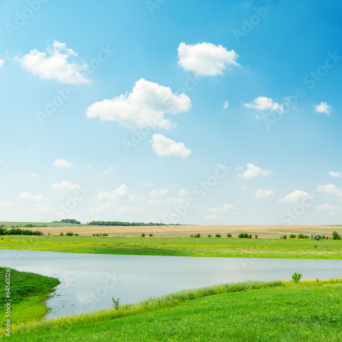 river in green grass under cloudy sky