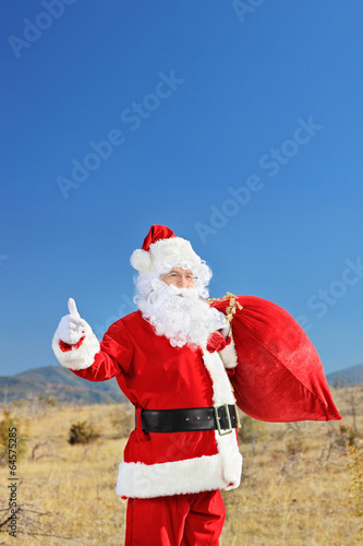 Santa hitchhiking outdoors with bag of presents