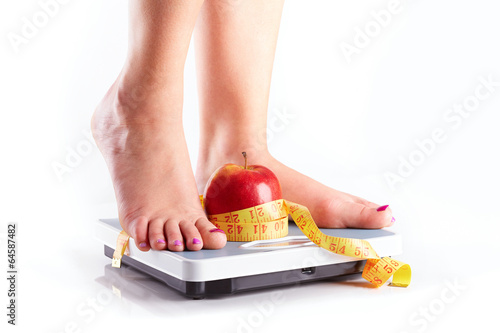 A pair of female feet standing on a bathroom scale with red appl photo