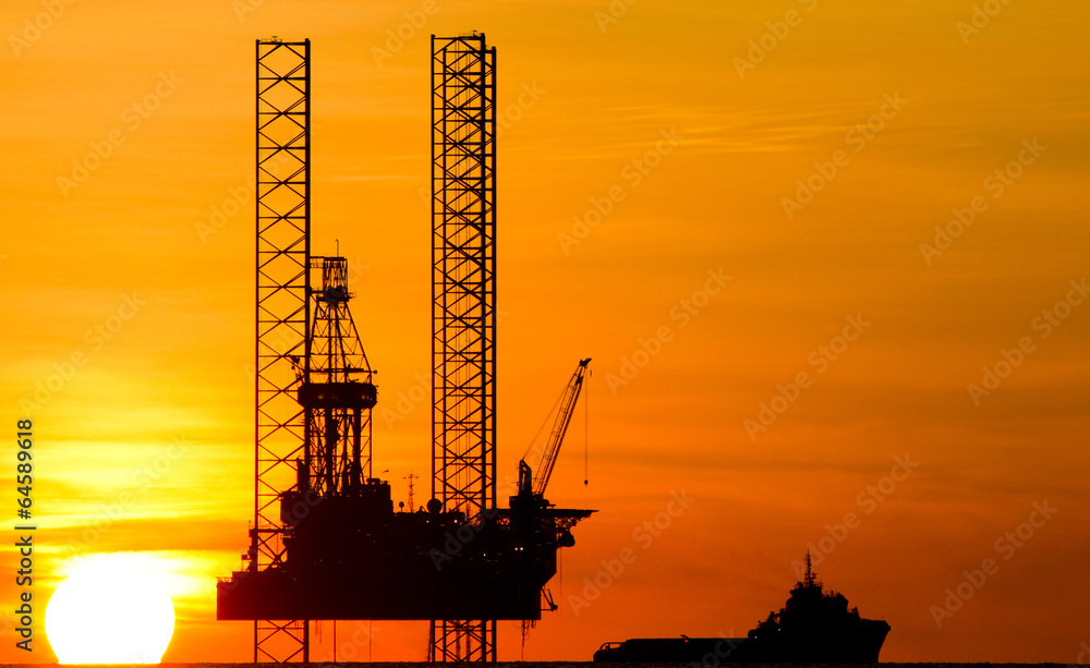 Offshore drilling rig and supply vessel at sunset
